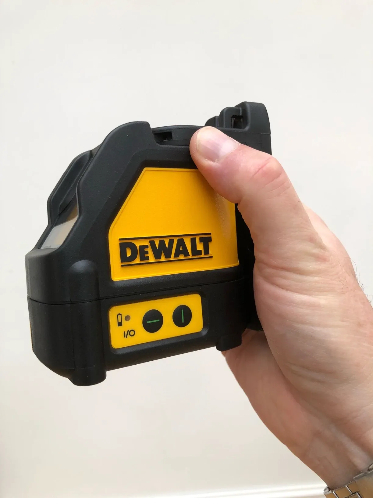 Hand holding a DEWALT self-levelling cross line laser tool with black and yellow housing against a plain light background.